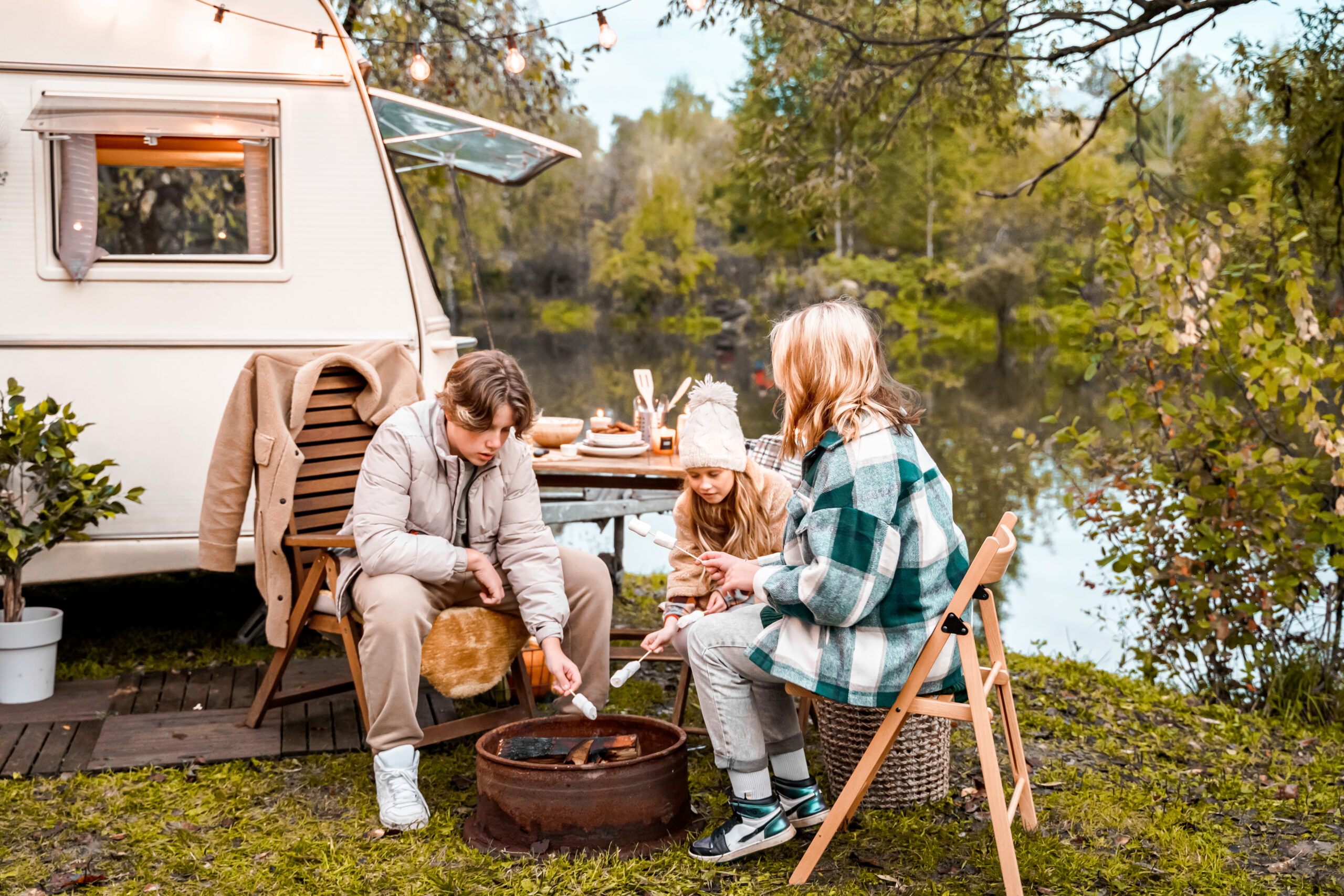 Children,family,brother sister fry marshmallows on fire. Picnic in nature. Wooden chair,table.Barbecue BBQ food. Holiday travel,vacation weekend dinner.Road lunch snack.Camper,house on wheels,trailer.